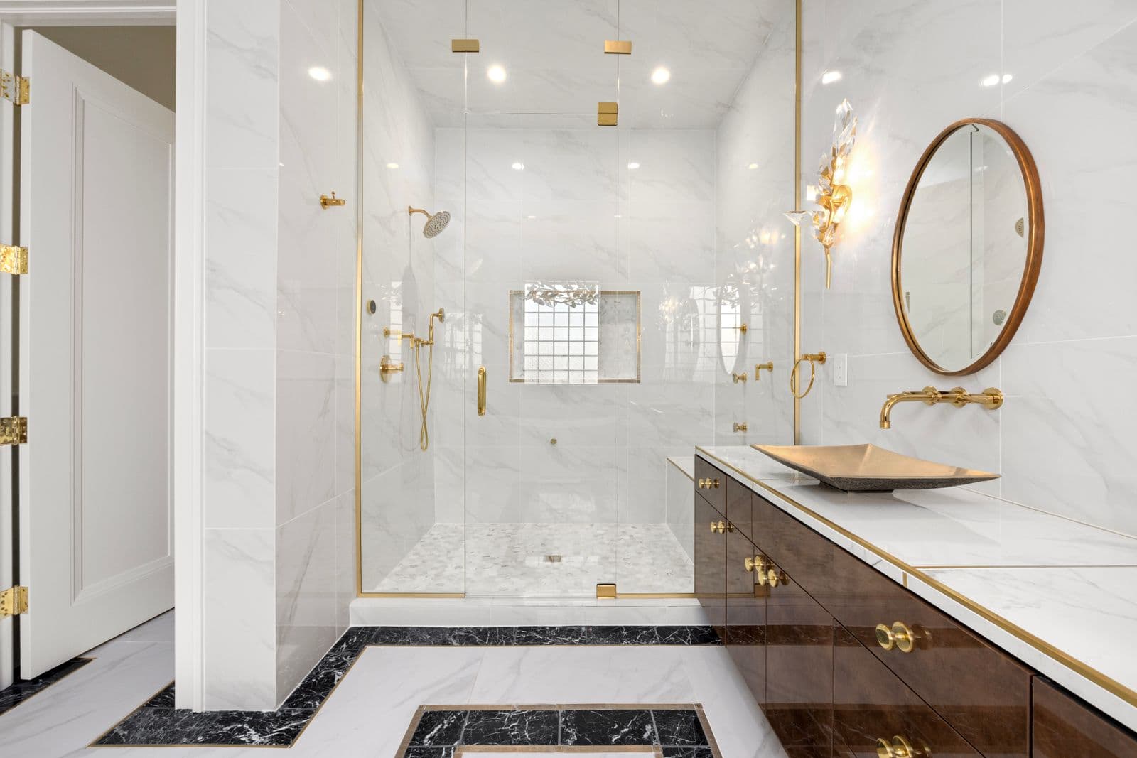 Luxury marble washroom with a brass rain shower, wall-mounted faucet, vessel basin and round mirror